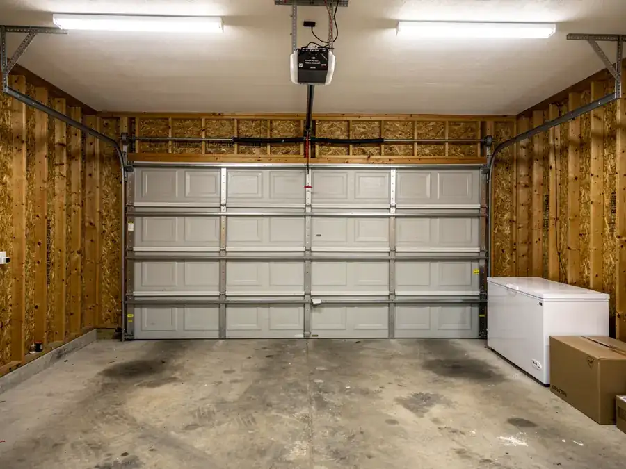 A closed garage door with an opener, fluorescent lights, and a white freezer.