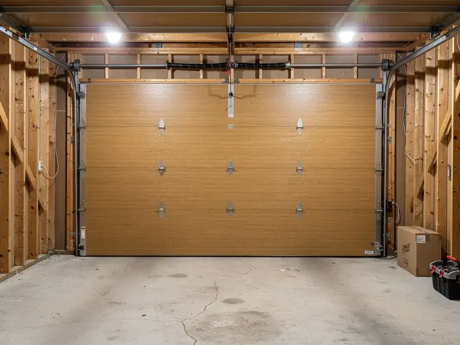 A closed light brown garage door with a torsion spring and tracks.